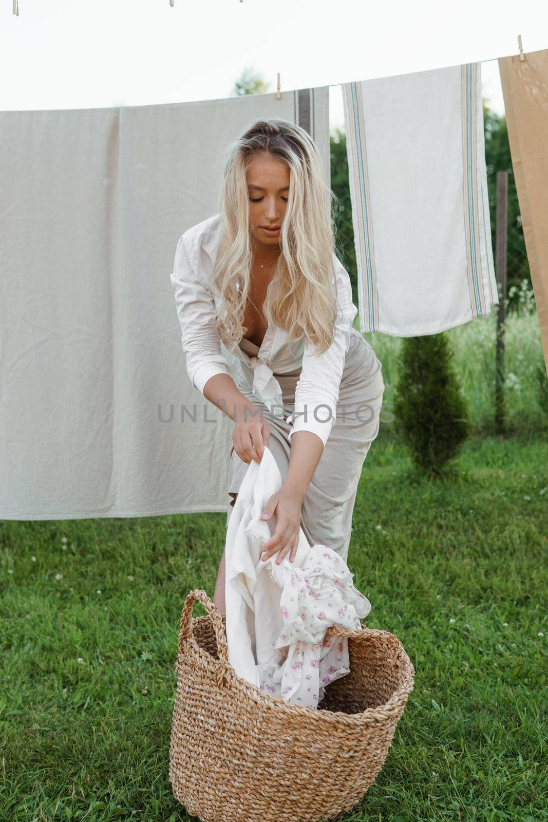 Laundry day. A woman hangs linen and towels on a tree in the courtyard of a village house. Summer cottage concept.