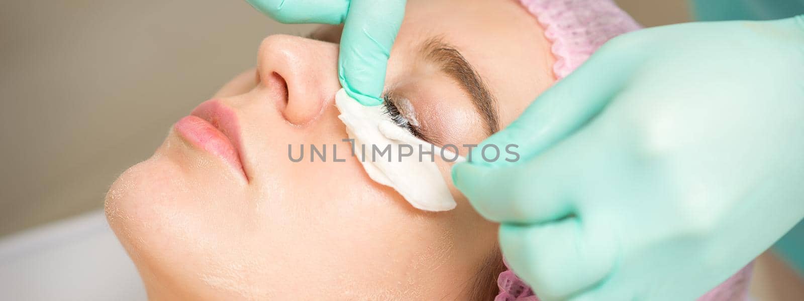 Young woman receiving eyelash removal procedure and removes mascara with a cotton swab and stick in a beauty salon
