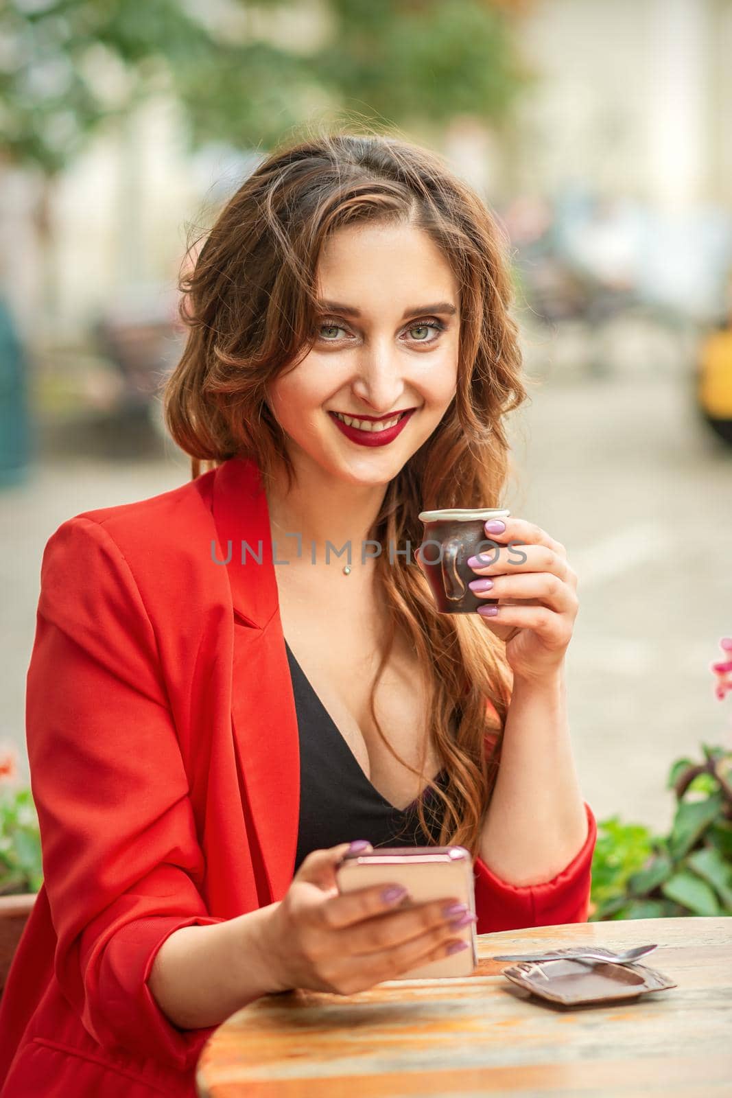 Tourist young caucasian woman in red jacket with coffee cup at the table in cafe outdoors