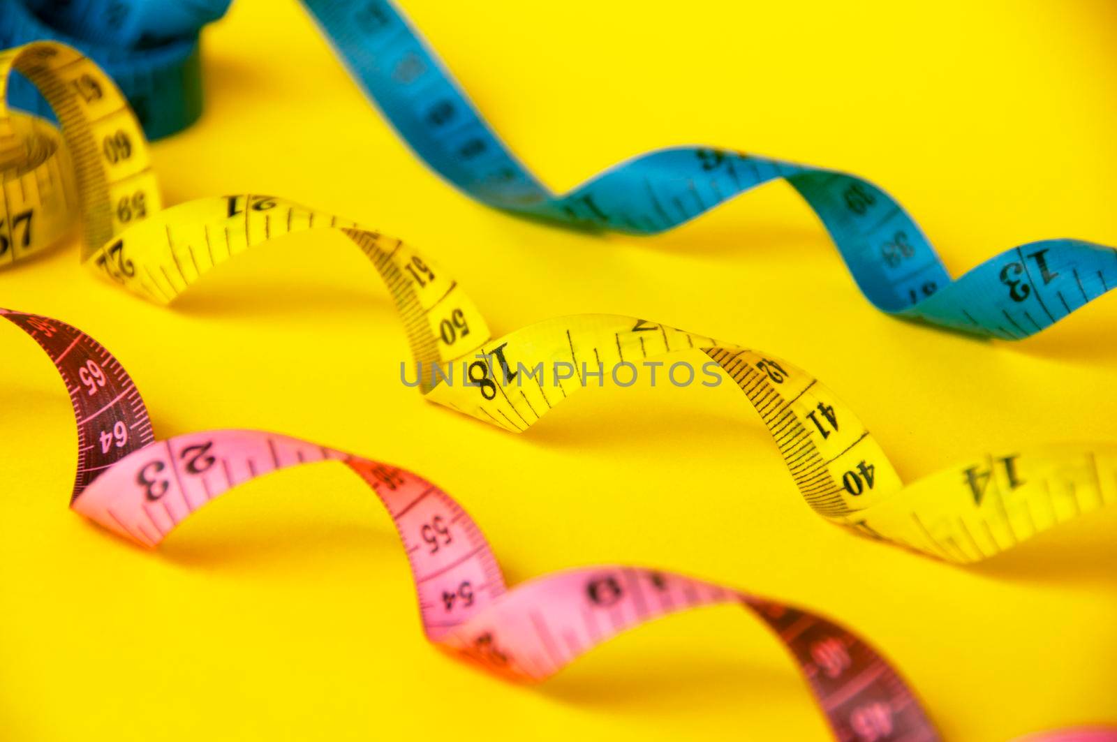 Red, yellow and blue measuring tapes on yellow cover background. Copy space and weight loss concept.