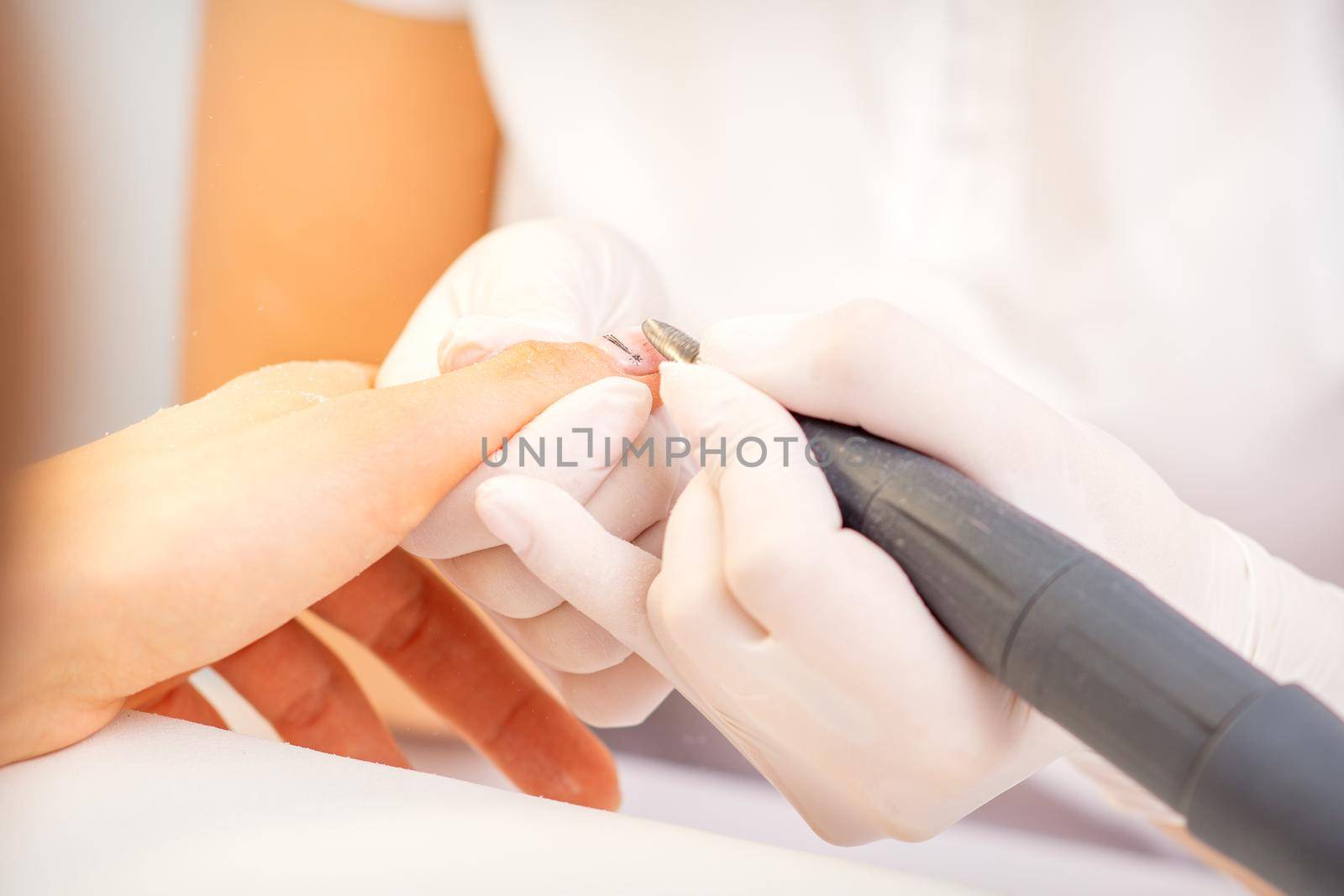 Closeup of manicure master in white gloves applying an electric nail file drill to remove the nail polish in the beauty salon