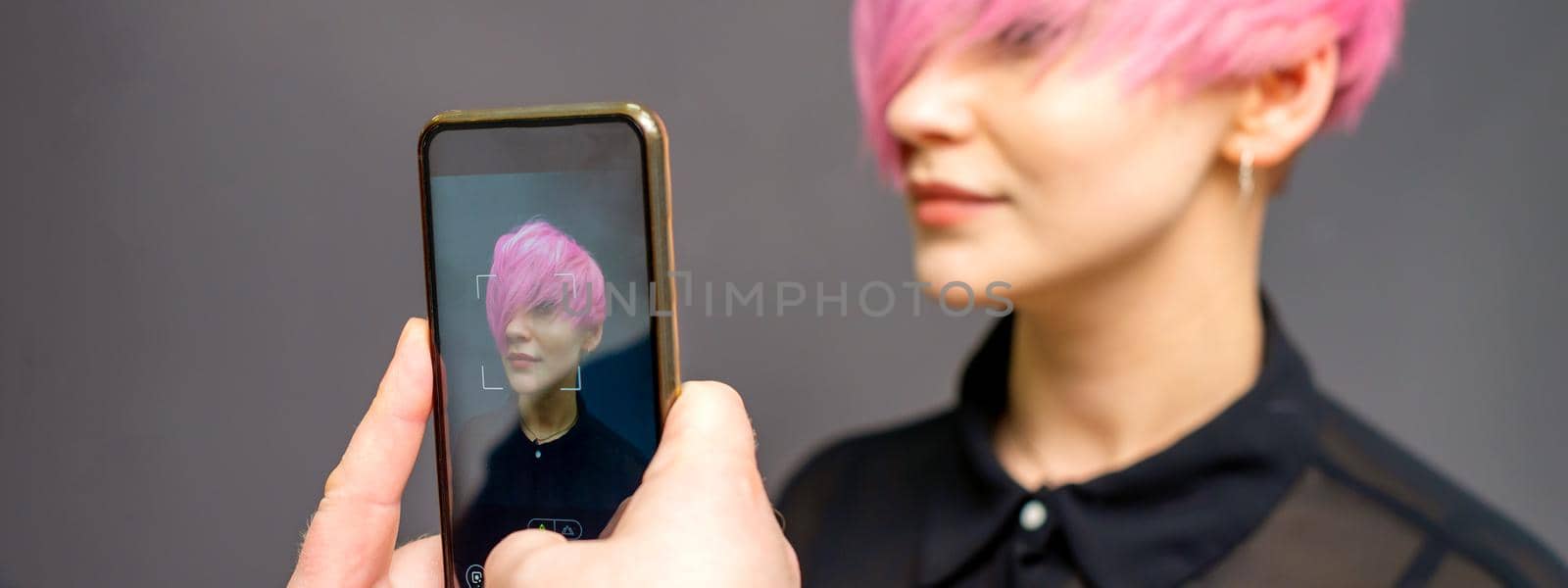 Man hairdresser's hands taking picture on smartphone of her client short pink hairstyle. by okskukuruza