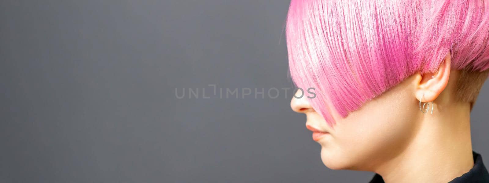 Profile portrait of a young caucasian woman with pink bob haircut isolated on a gray background, copy space. by okskukuruza