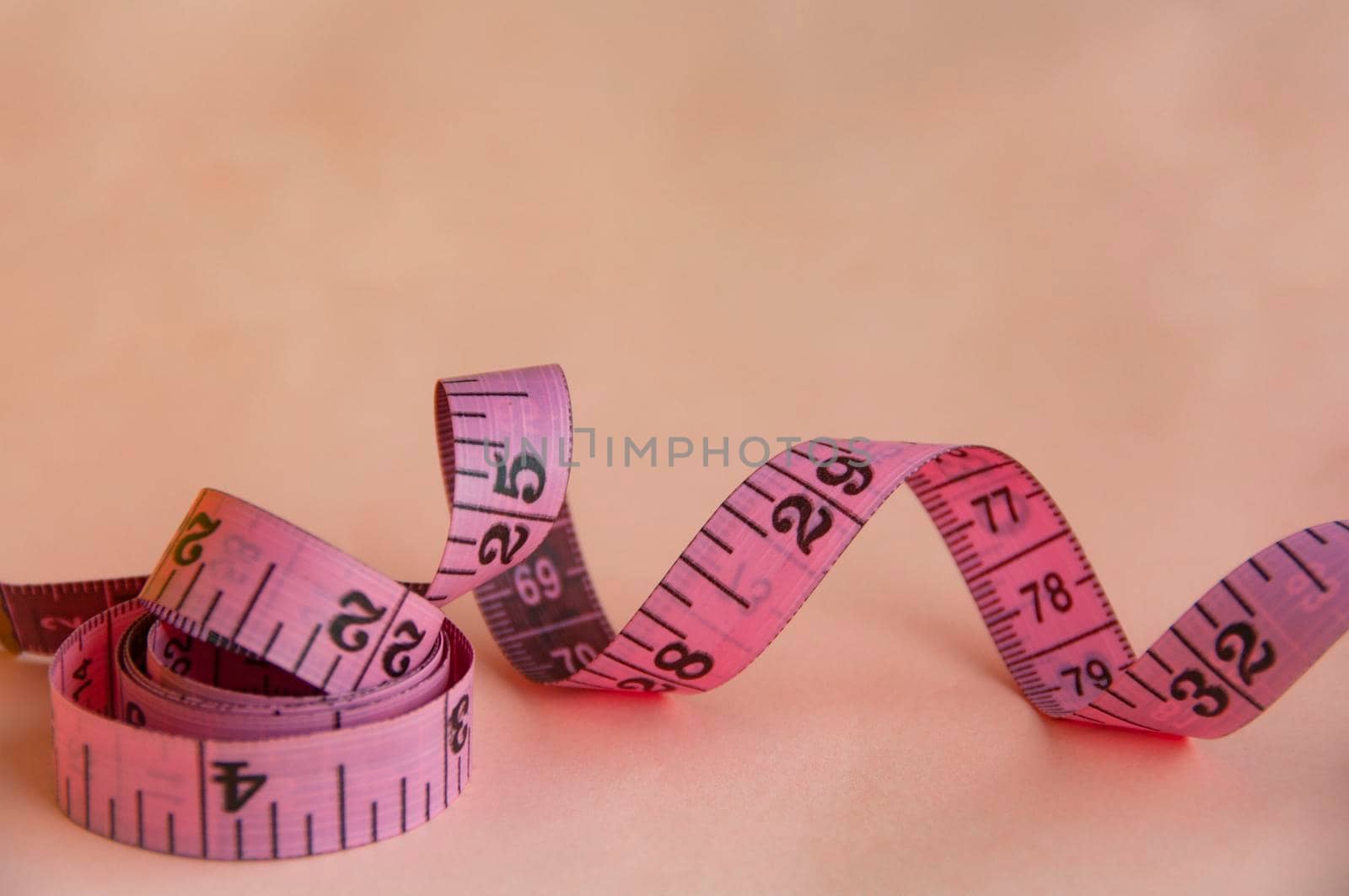 Red measuring tapes on pink cover background with customizable space for text or ideas. Copy space and weight loss concept.