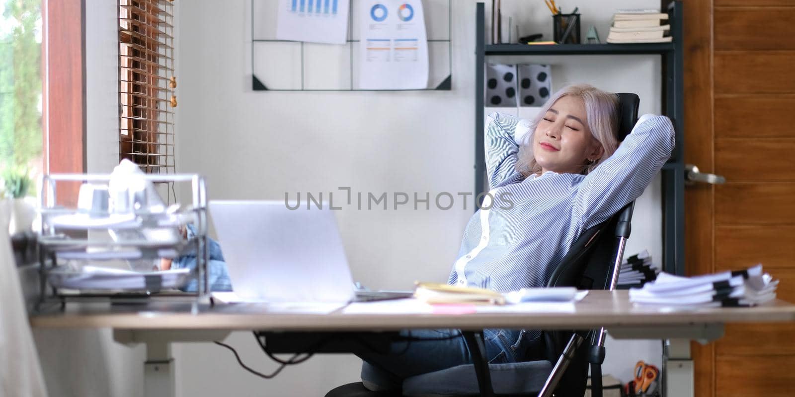Business asian woman relaxing with hands behind her head and sitting on an office chair.