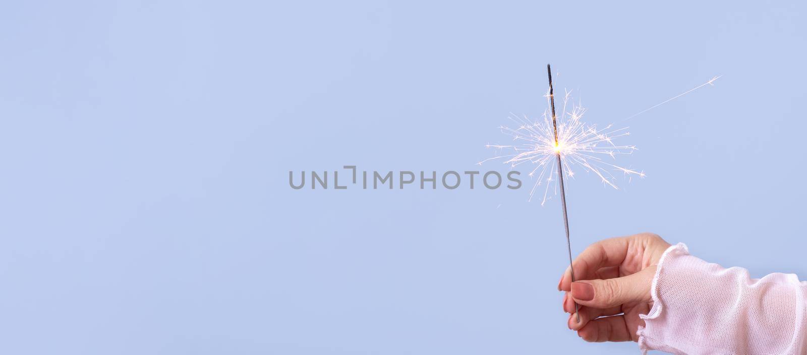 sparklers in a woman's hand on a blue background with copy space. Christmas holiday concept by ssvimaliss
