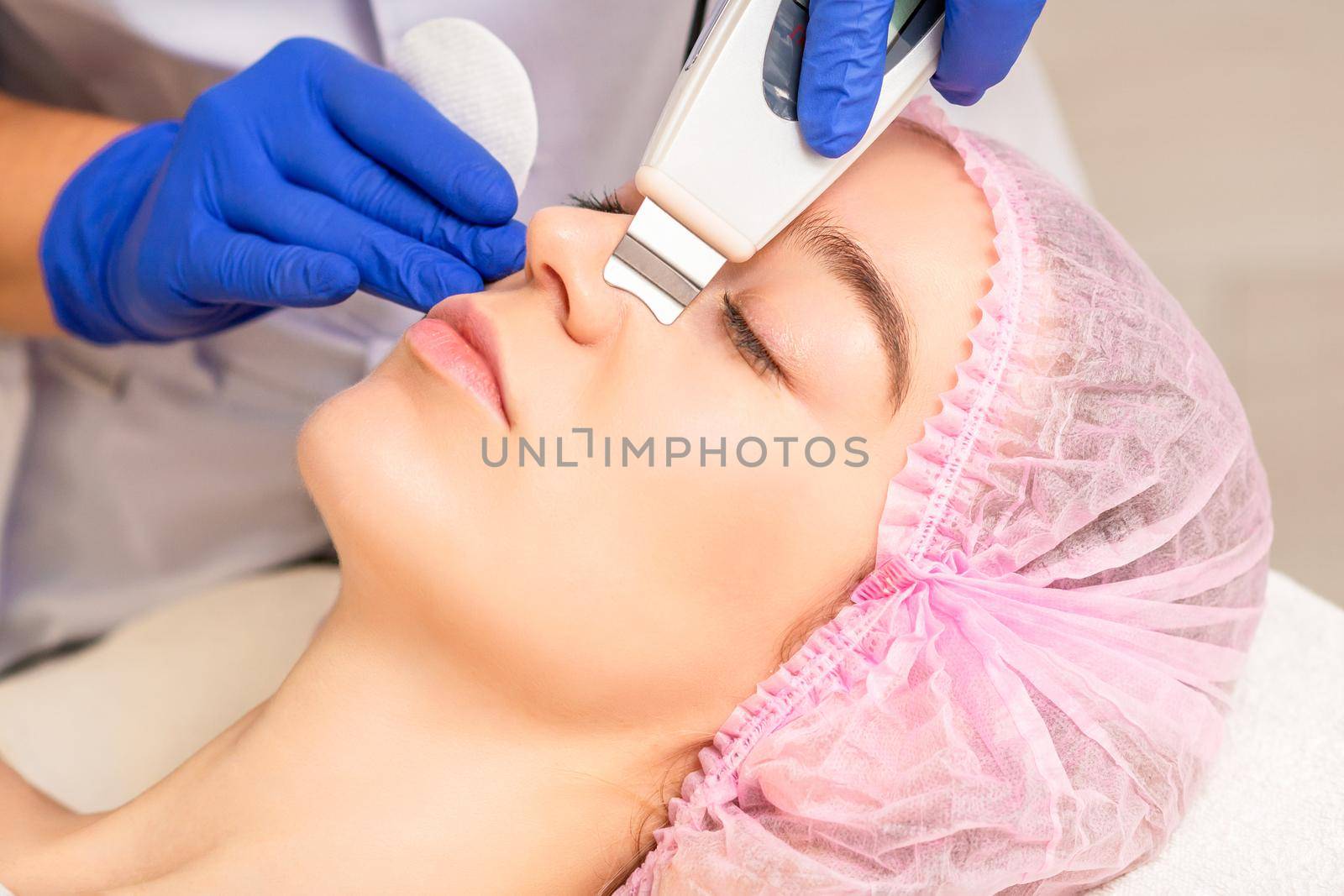 Closeup of beautiful young woman receiving ultrasound facial exfoliation and cavitation facial peeling with ultrasonic equipment in cosmetology office