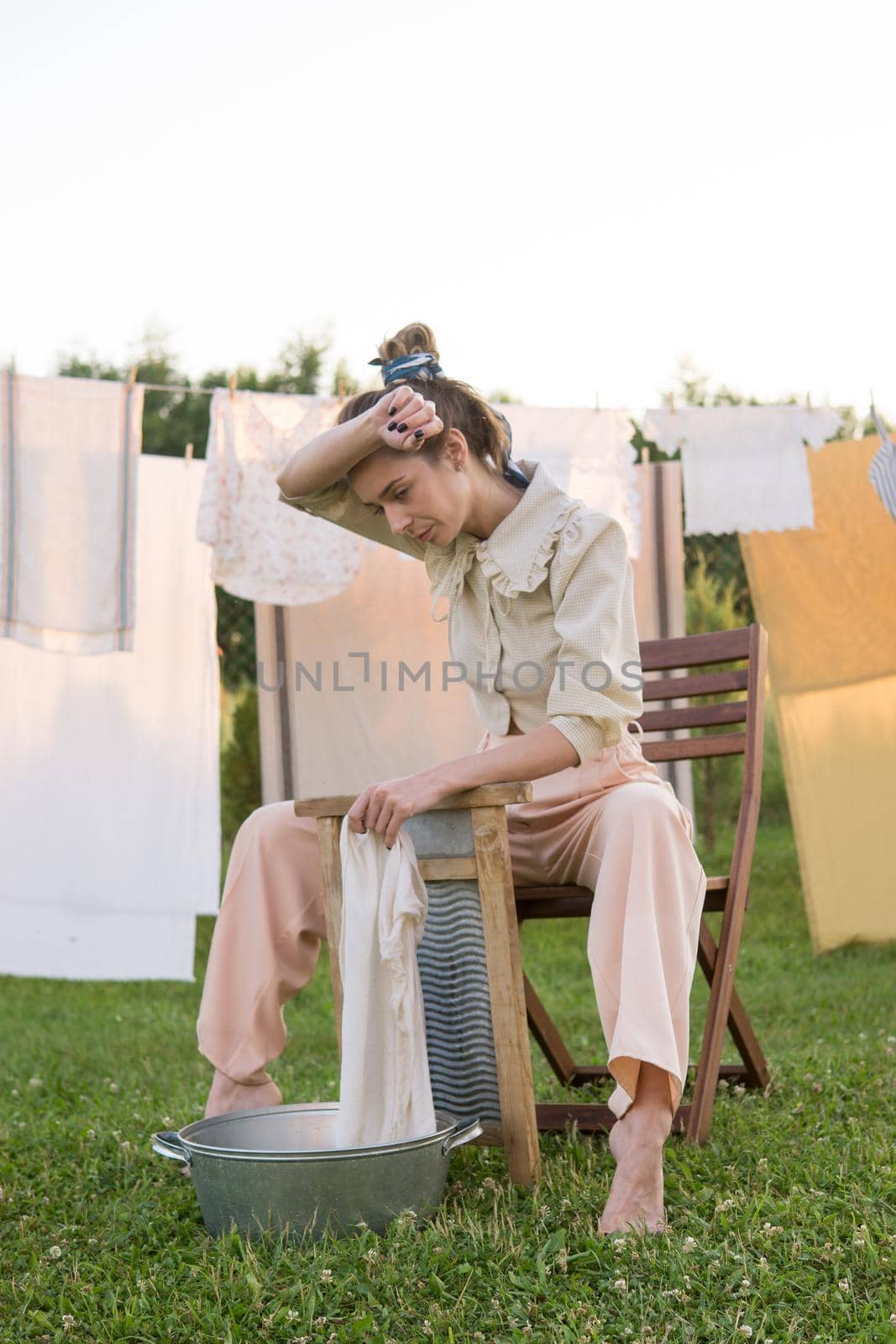 Laundry day. A woman hangs linen and towels on a tree in the courtyard of a village house. Summer cottage concept.