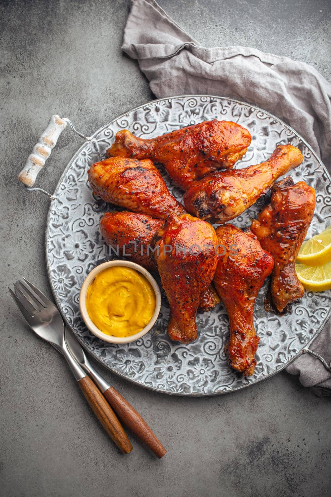 Traditional Indian dish Tandoori chicken legs served with exotic yellow sauce and lemon wedges on rustic aluminum plate on grey concrete background from above