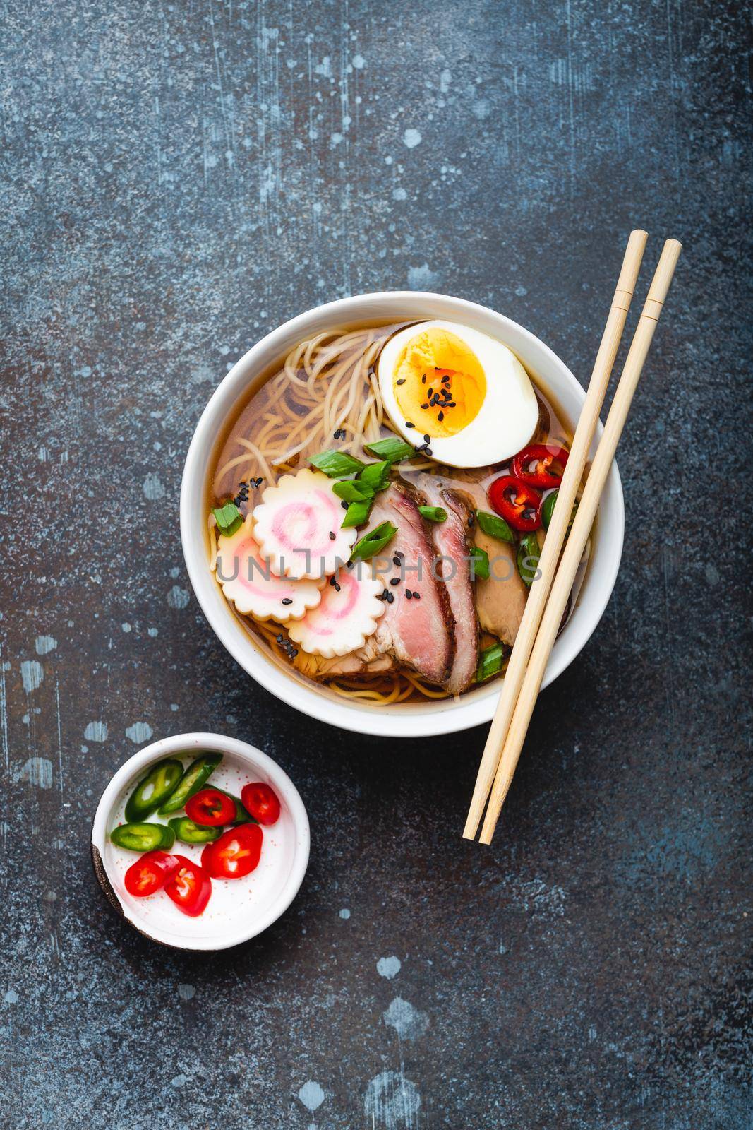 Tasty Japanese noodle soup ramen in white ceramic bowl with meat broth, sliced pork, narutomaki, egg with yolk on rustic stone background. Traditional dish of Japan, top view, close-up, concept