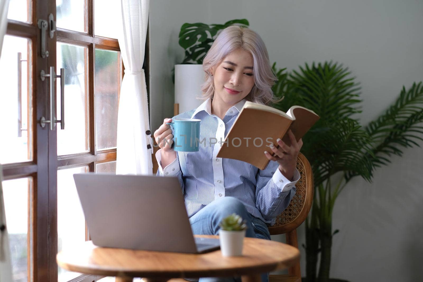 Portrait Asian woman reading book and relaxing with coffee at home by wichayada