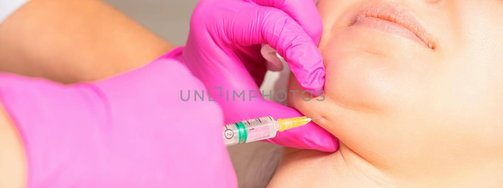 The cosmetologist makes lipolytic injection on the chin of a young woman against the double chin in a beauty salon. by okskukuruza