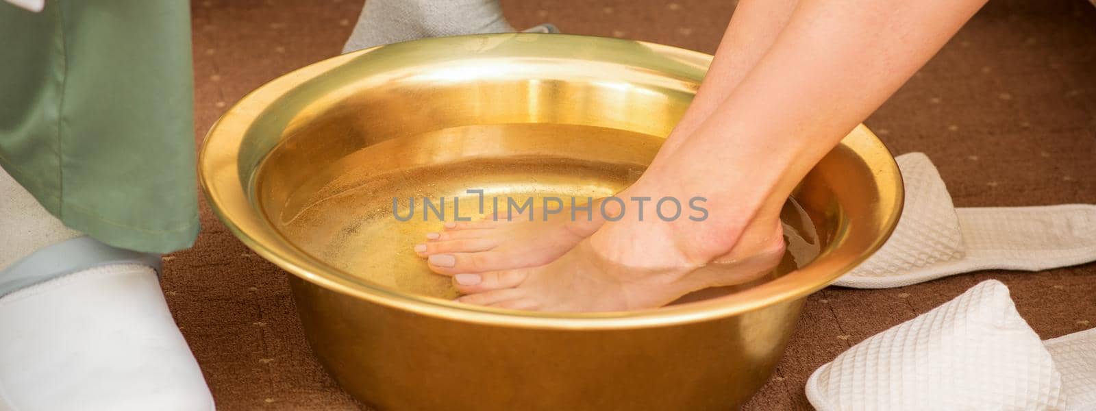 Female feet in a golden bowl with water in spa salon. Spa treatment