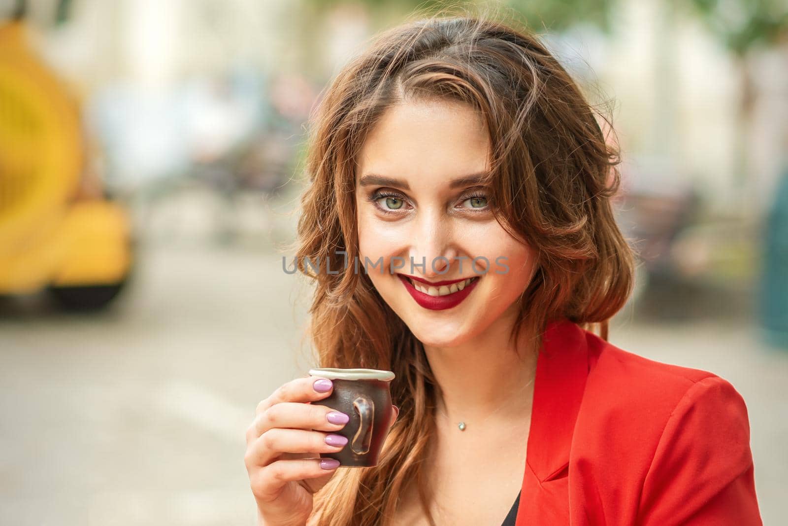 Tourist young caucasian woman in red jacket with coffee cup at the table in cafe outdoors