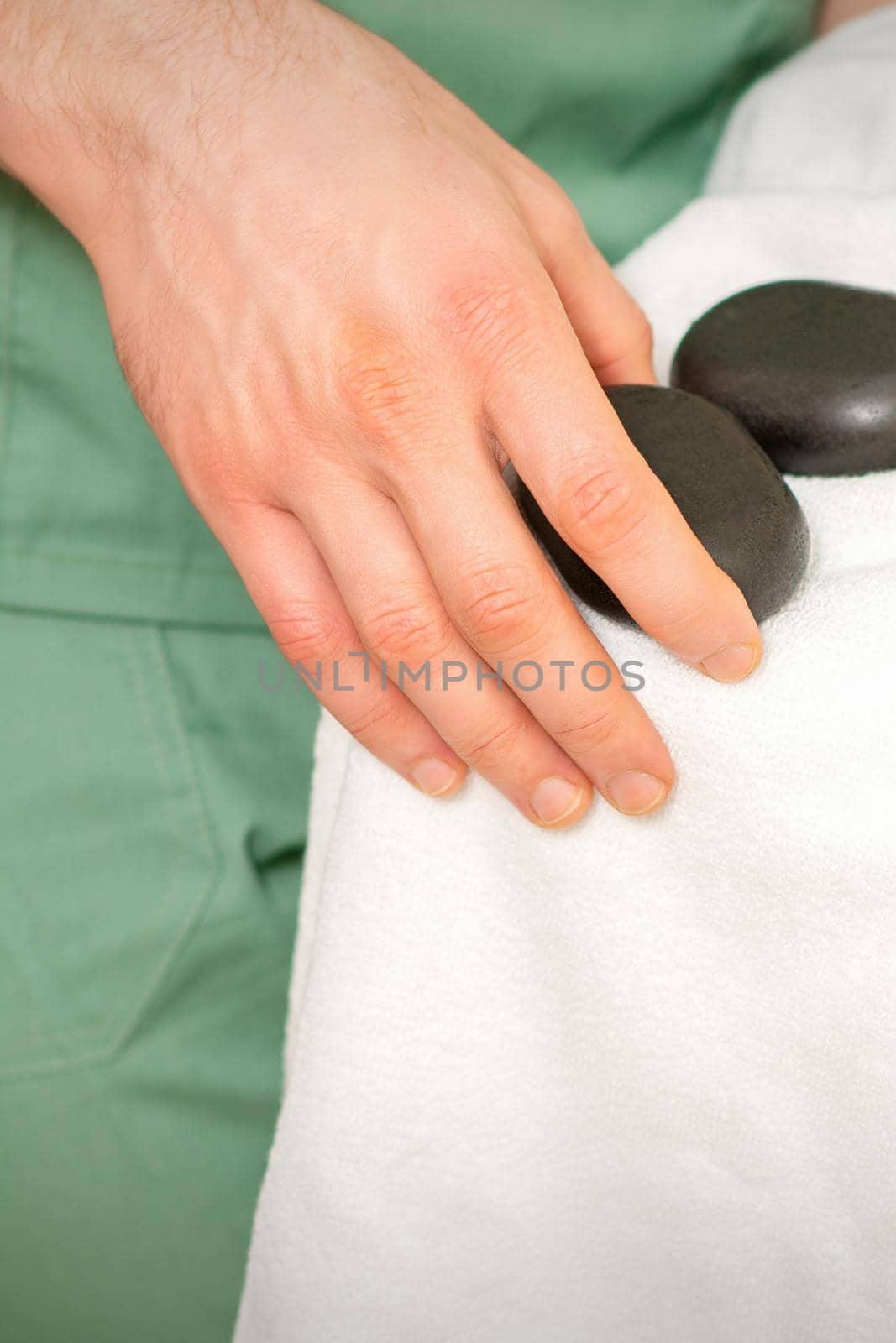 Close up of masseur's hand wipes black massage stones with a white towel