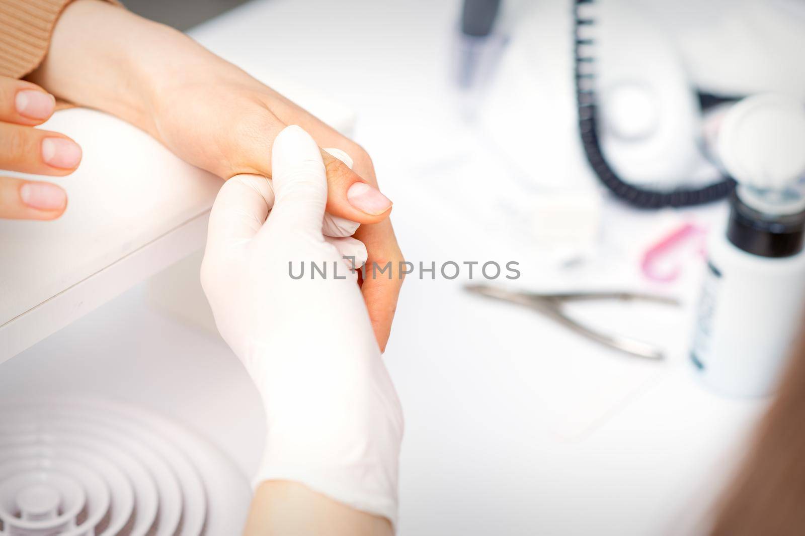 The manicurist holds the female thumb during a manicure procedure in the nail salon