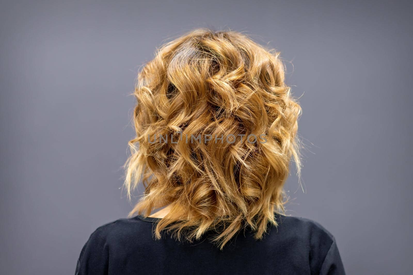 Back view of the woman with long brown curly hair stands on a dark background