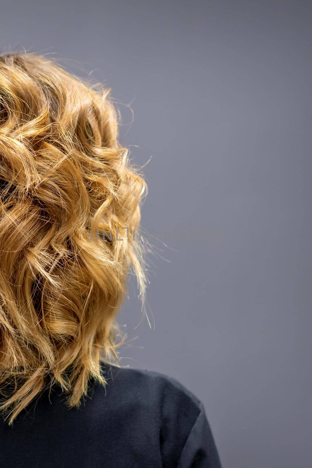 Back view of the woman with long brown curly hair stands on a dark background