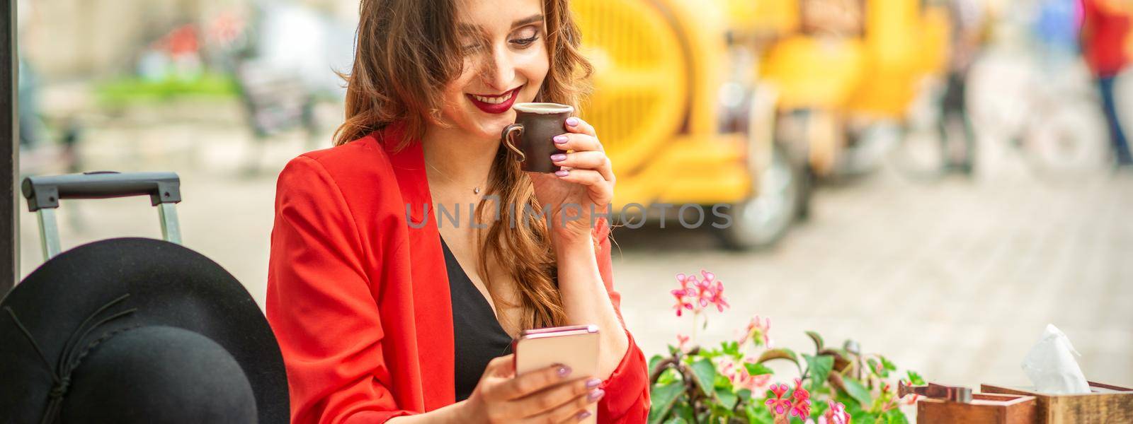 Tourist young caucasian woman in red jacket with coffee cup at the table in cafe outdoors