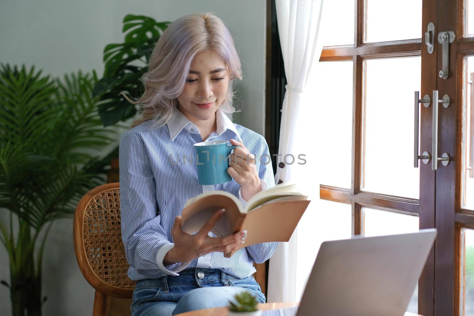 Asian woman reading a book and drinking coffee in the morning..