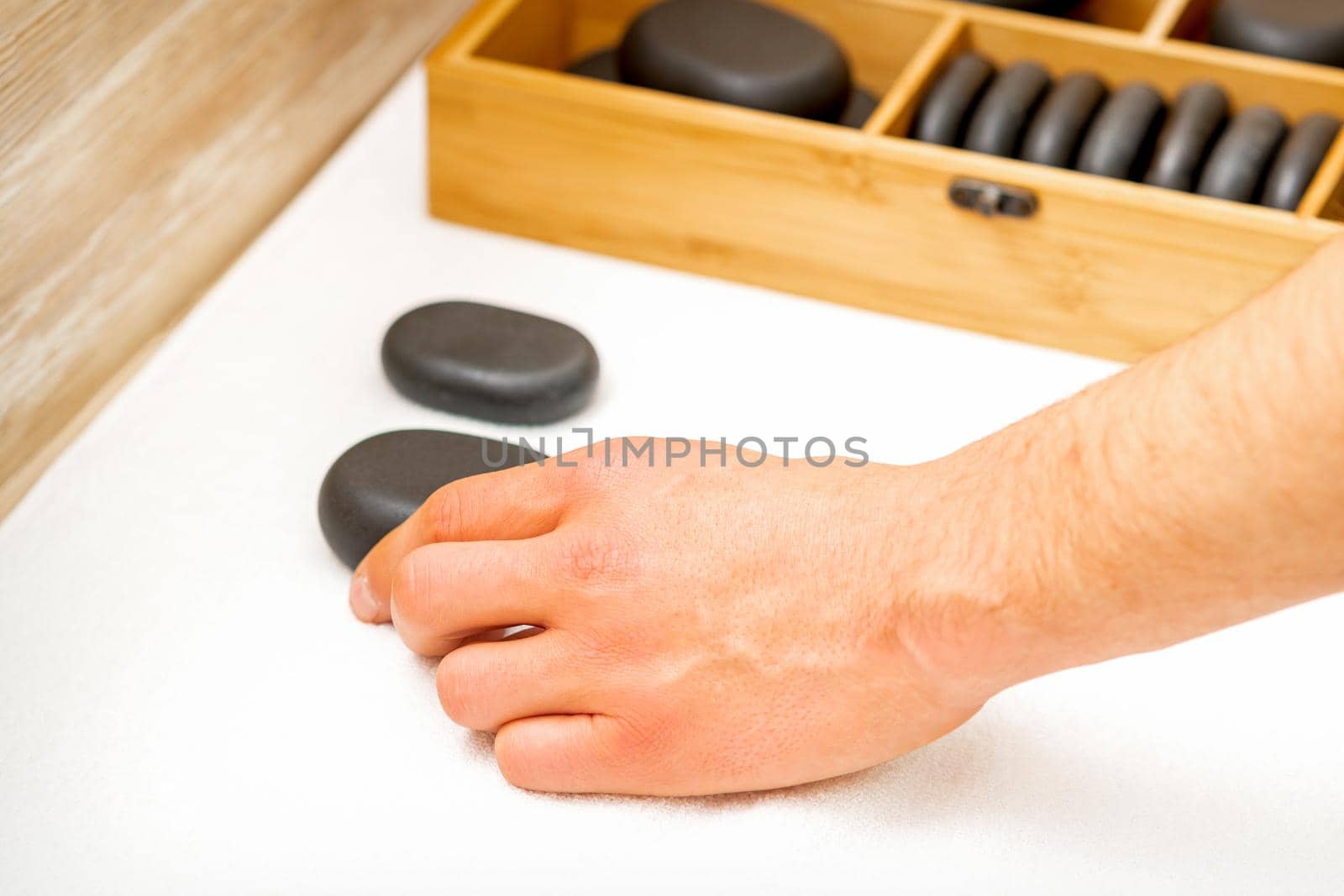 Hand of masseur takes black massage stones from the table in spa salon