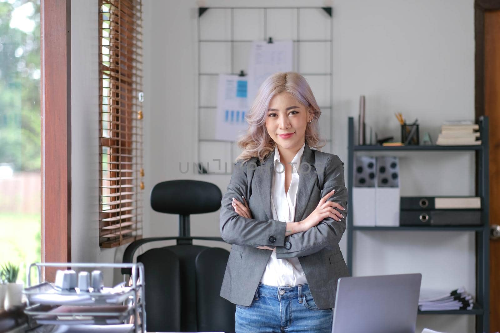 Young confident smiling Asian business woman leader, successful entrepreneur, elegant professional company executive ceo manager. Asian business woman is standing in office with arms crossed..