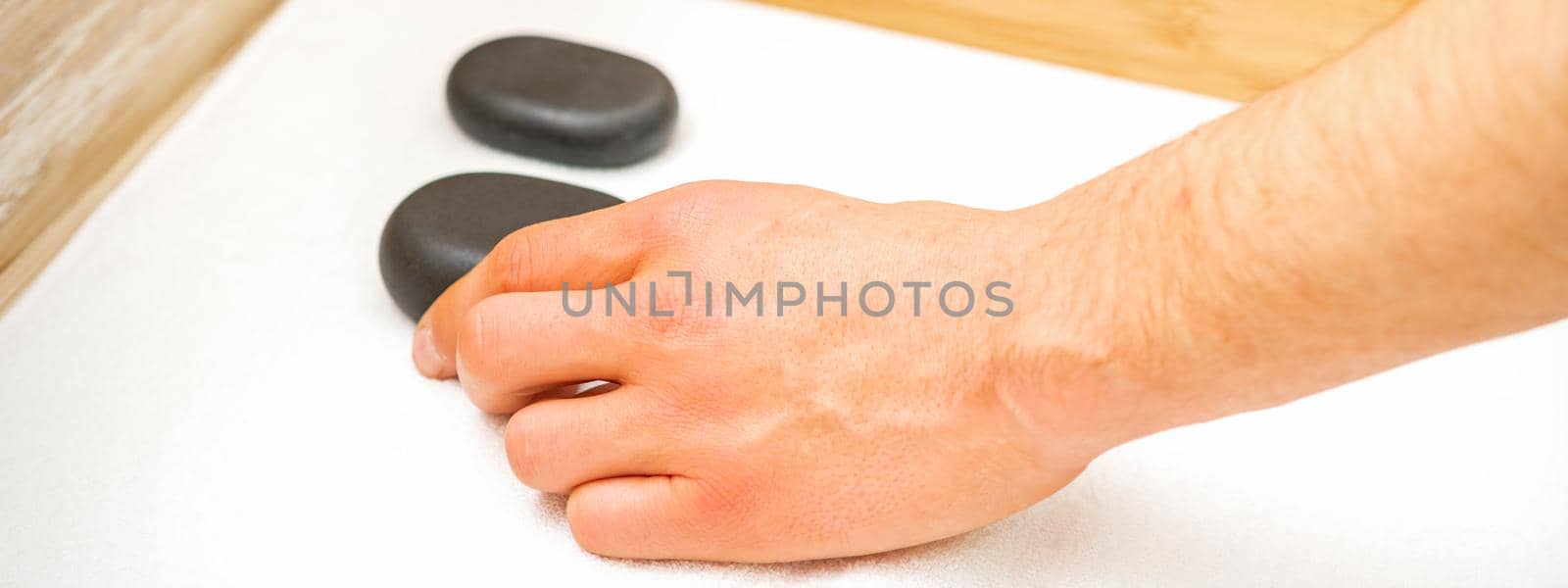 Hand of masseur takes black massage stones from the table in spa salon