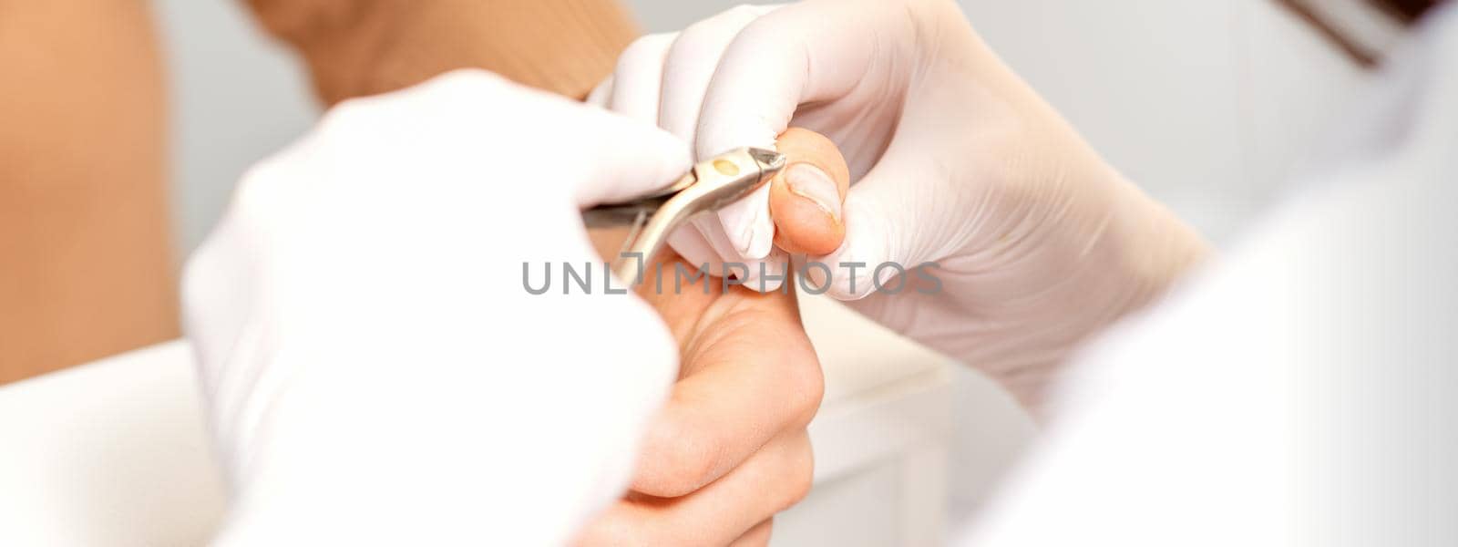 Close up of manicure master with manicure nipper cuts cuticles of female nails at beauty salon