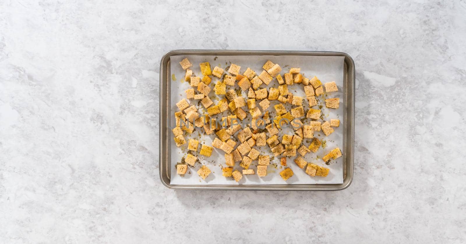 Flat lay. Baking croutons seasoned with olive oil and spiced on a baking sheet lined with parchment paper.