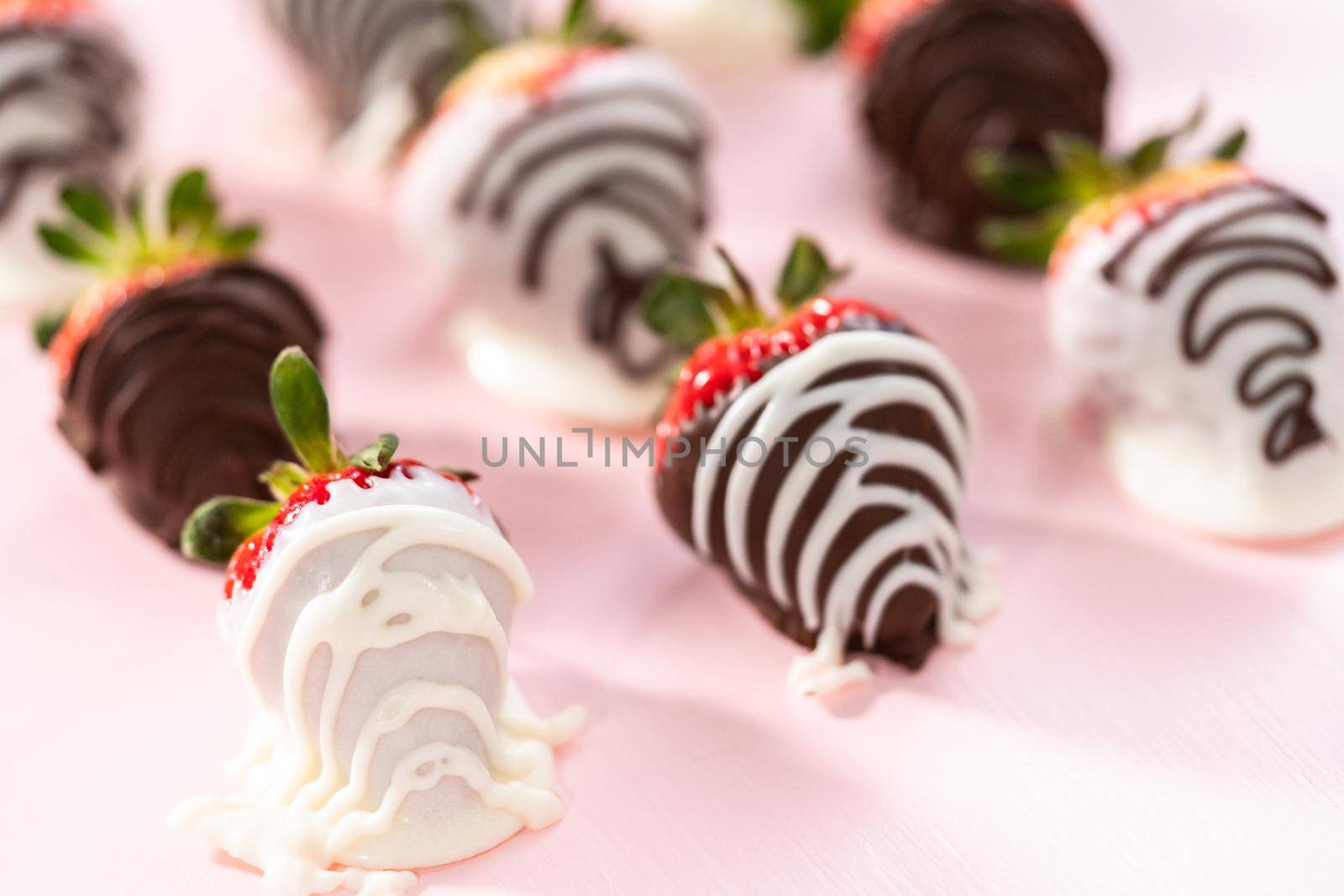 White and dark chocolate dipped strawberries on a pink background.