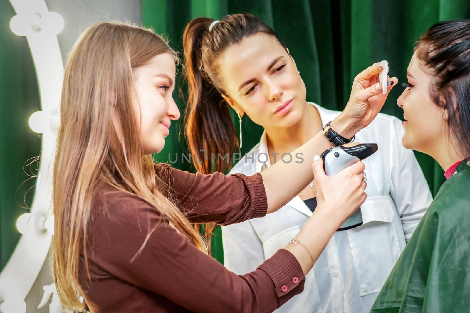 Makeup artist making professional makeup on the face of a young woman using an airbrush. by okskukuruza