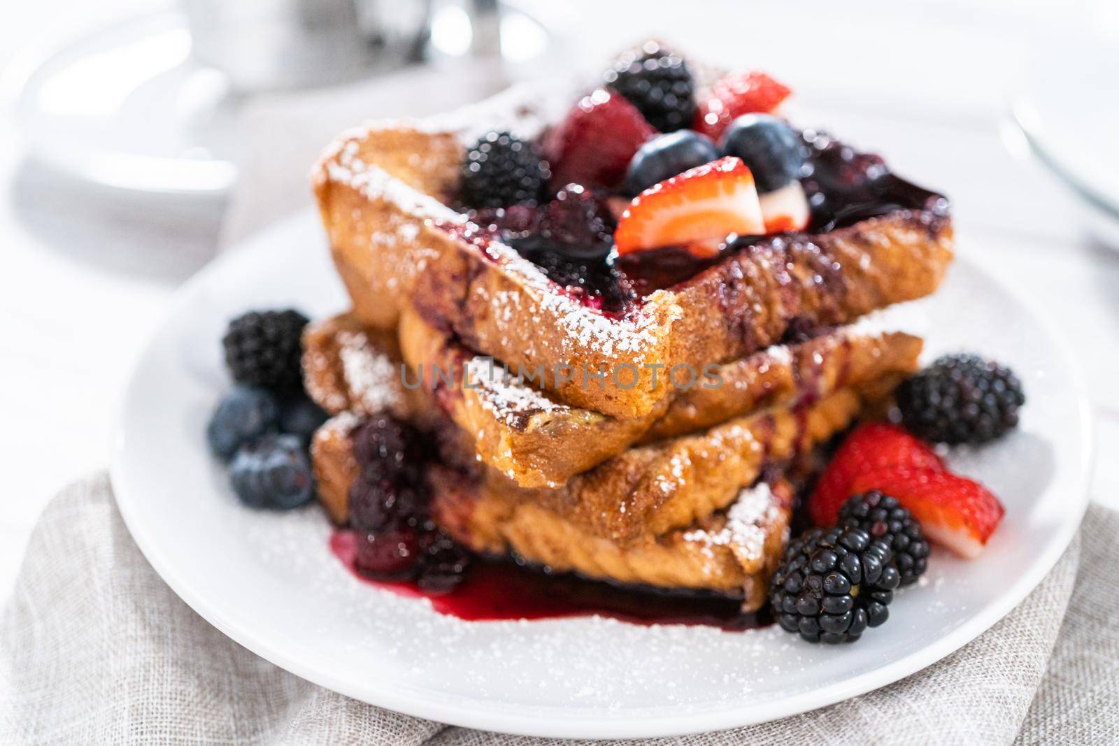 Stack of freshly made french toast garnished with mix berry compote and powder sugar.