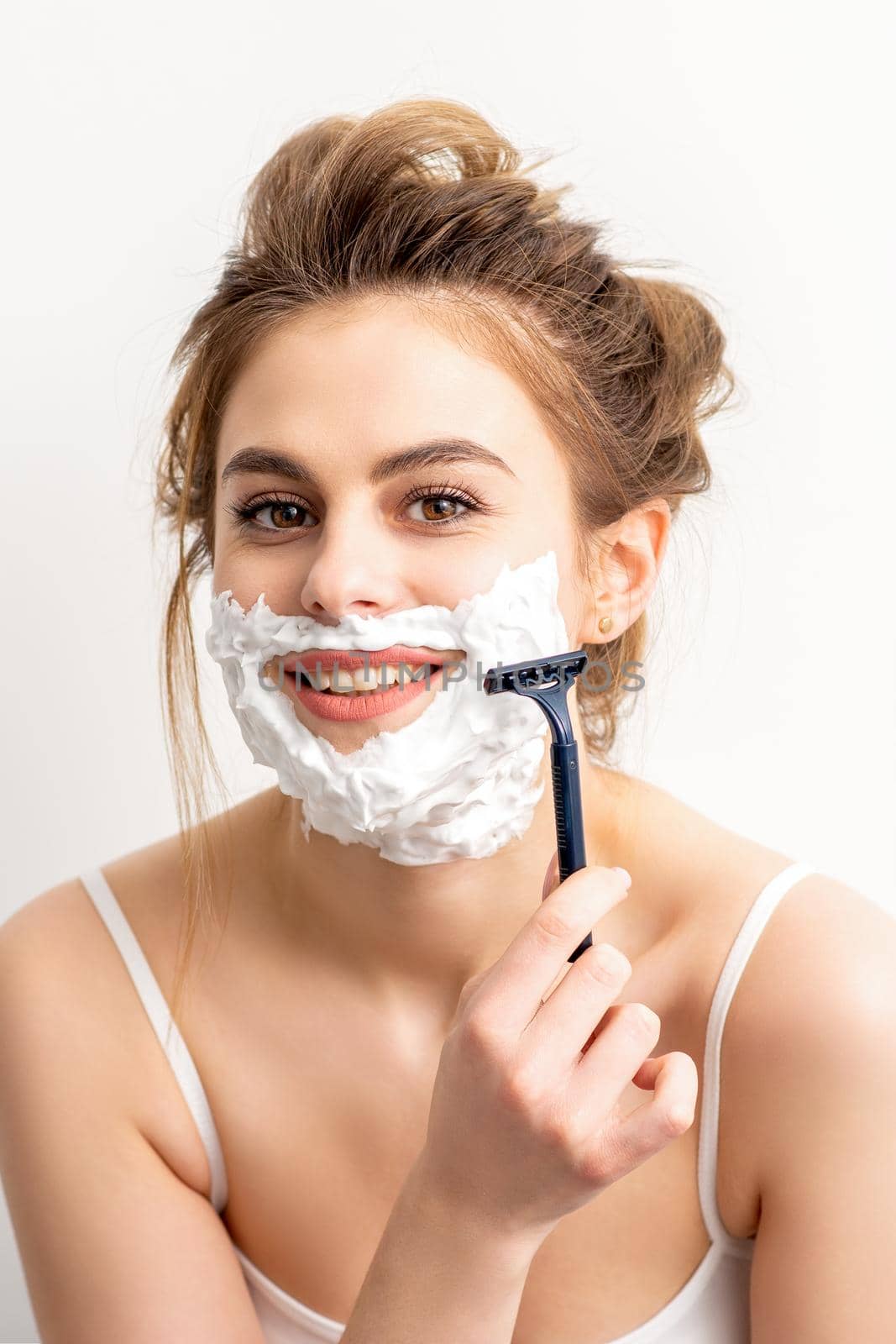Portrait of beautiful young smiling caucasian woman shaves face with razor on white background