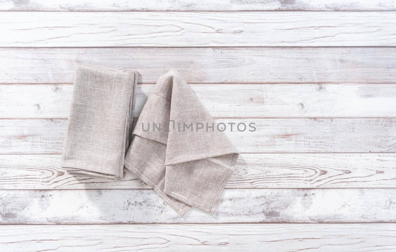 Flat lay. Folding a natural color linen dinner napkin on a white wooden table.