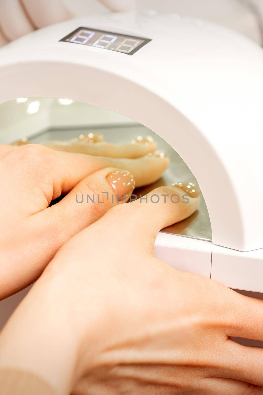 Female hand with manicured fingers dry inside UV light machine in manicure salon