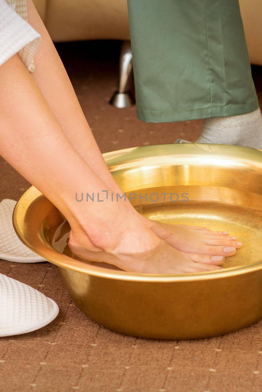 Female feet in a golden bowl with water in spa salon. Spa treatment