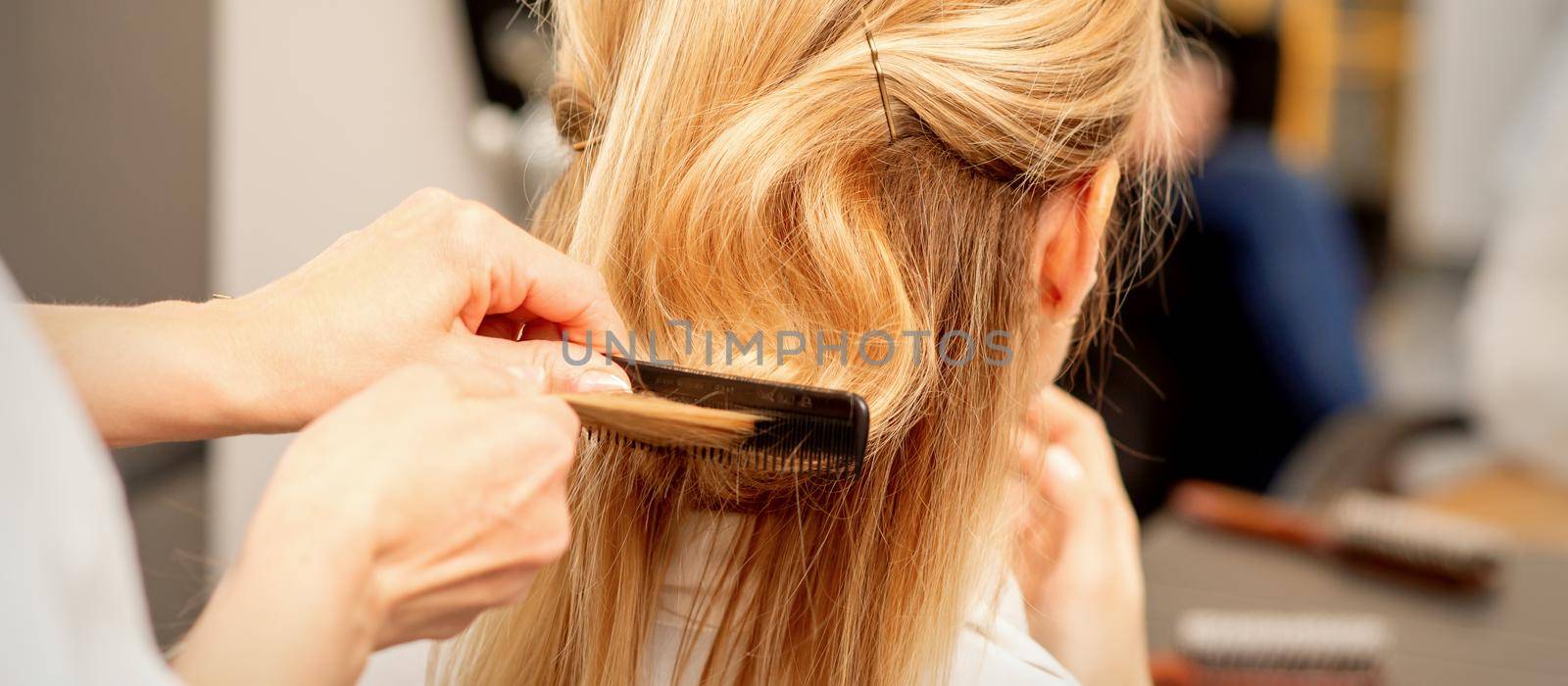 A hairdresser is combing female hairstyling in a hairdressing beauty salon. by okskukuruza