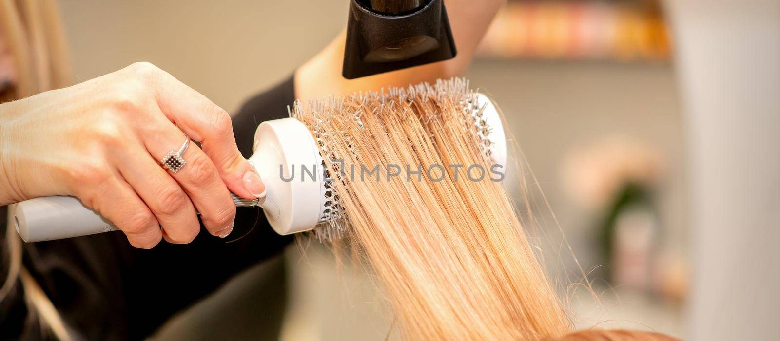 Professional hairdresser dry hair with a hairdryer and round hairbrush in a beauty salon. by okskukuruza