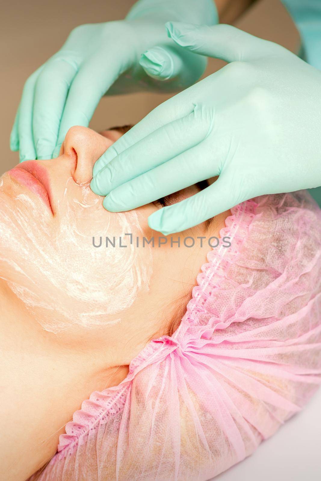 A cosmetologist is applying cream on the female face, close-up view. Woman with doctor beautician in beauty clinic