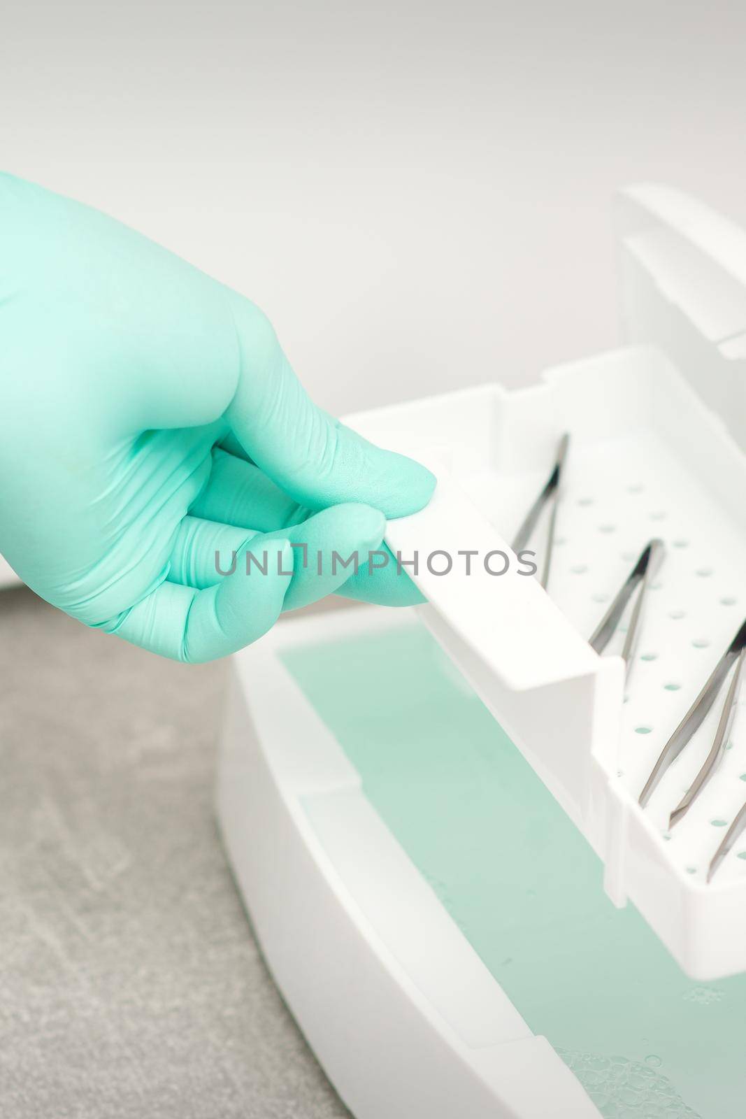 The beautician holds a tray of tweezers preparing them for disinfection with a special liquid and machine
