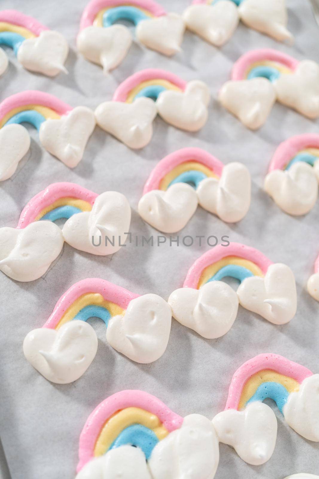 Freshly baked unicorn theme meringue pops cooling on baking sheets lined with parchment paper.