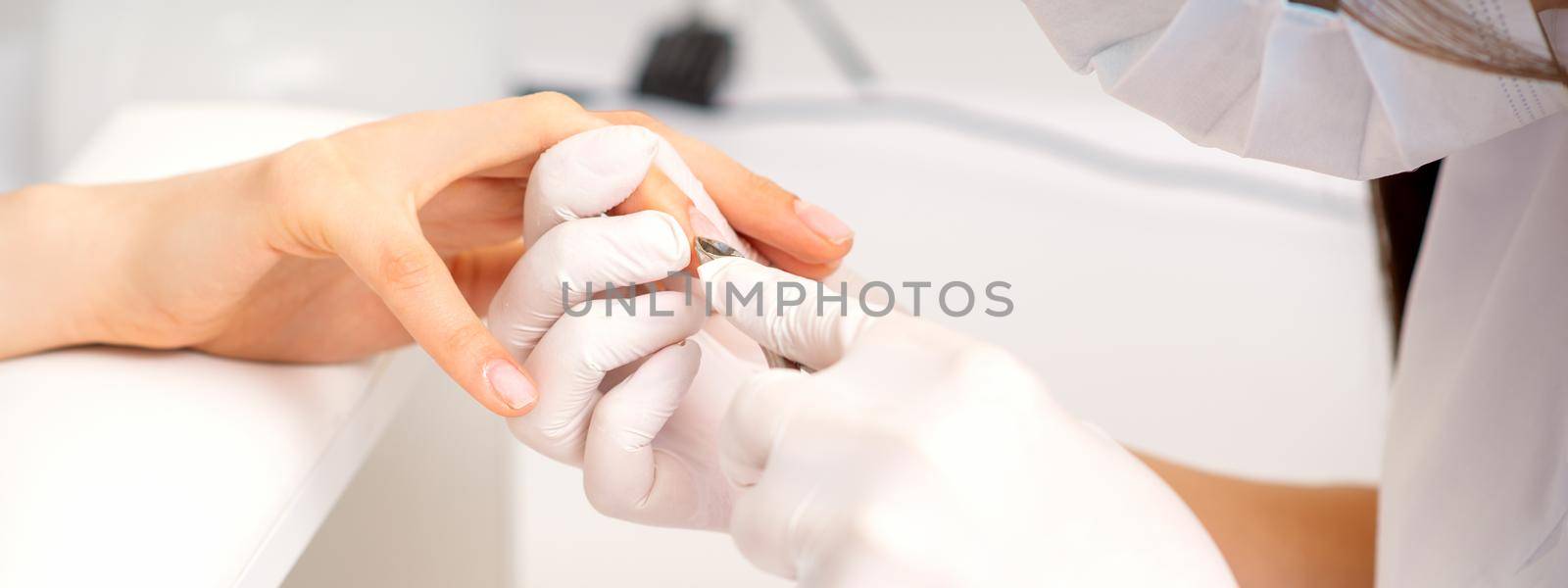 Close up of manicure master with manicure nipper cuts cuticles of female nails at beauty salon