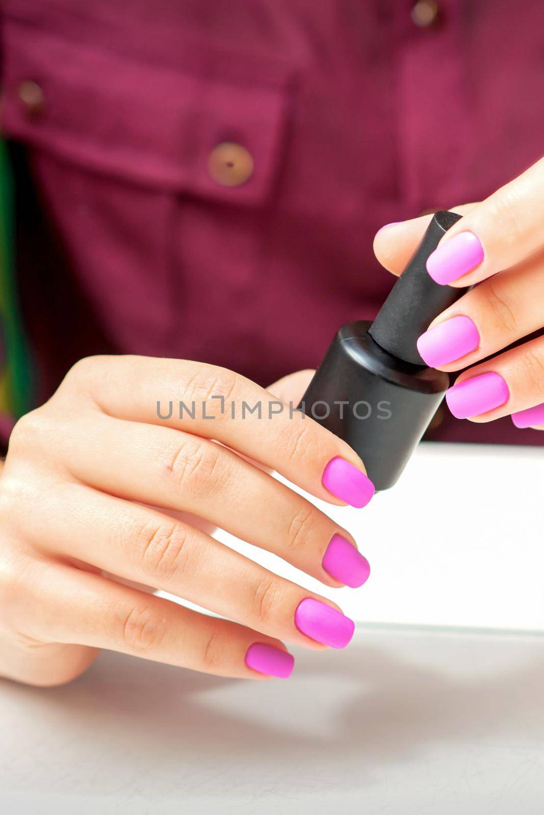 White woman holding nail polish black bottle with painted pink nails close up