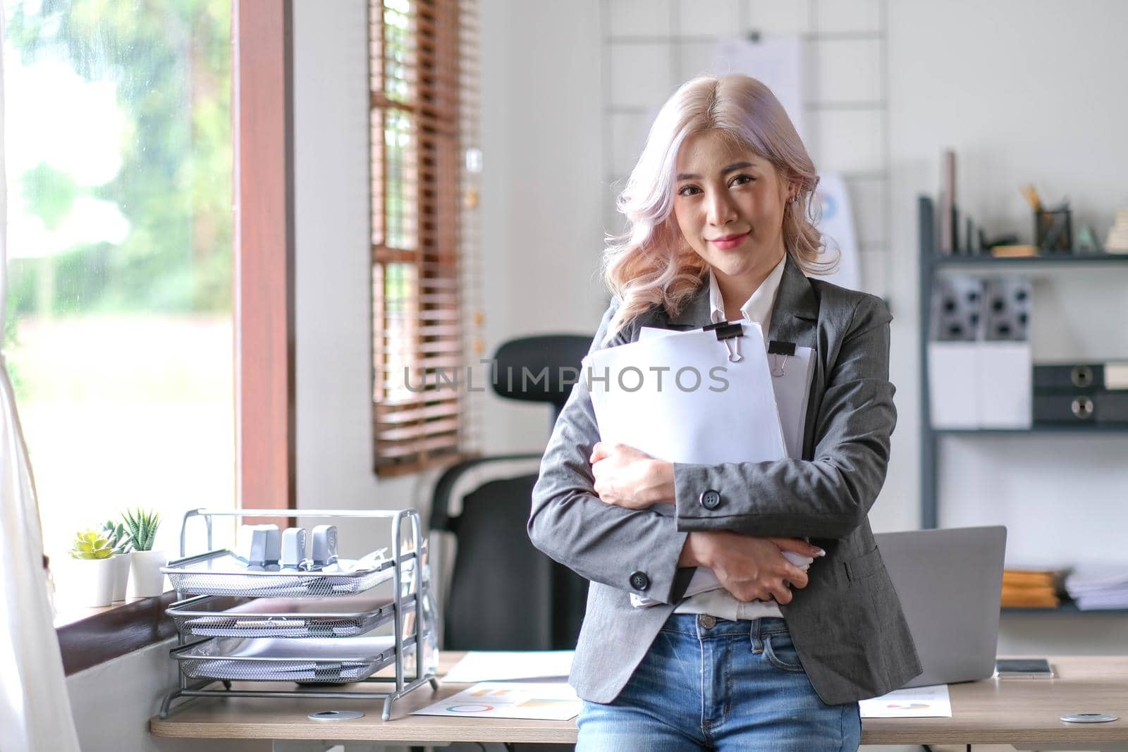 Charming Asian woman with a smile standing holding papers at the office..