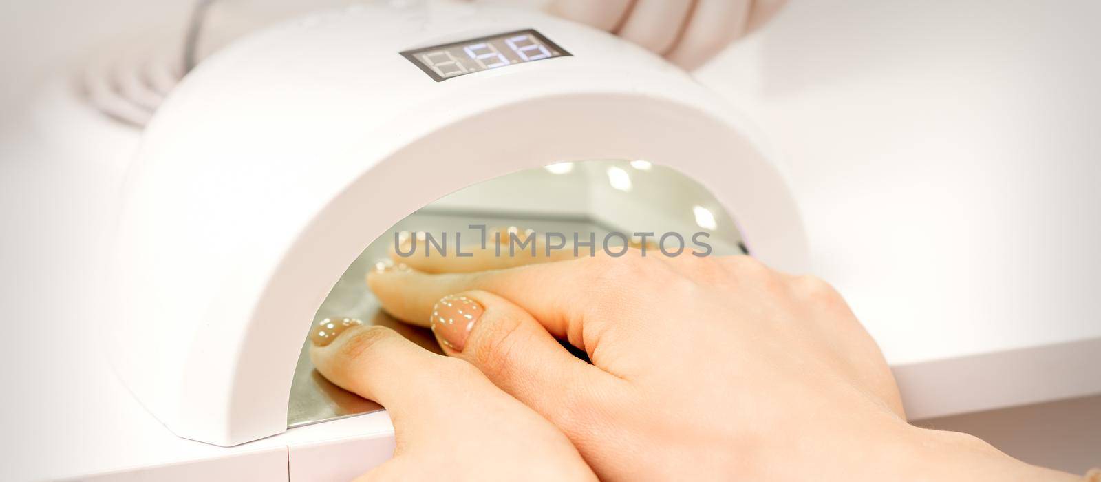 Female hand with manicured fingers dry inside UV light machine in manicure salon. by okskukuruza