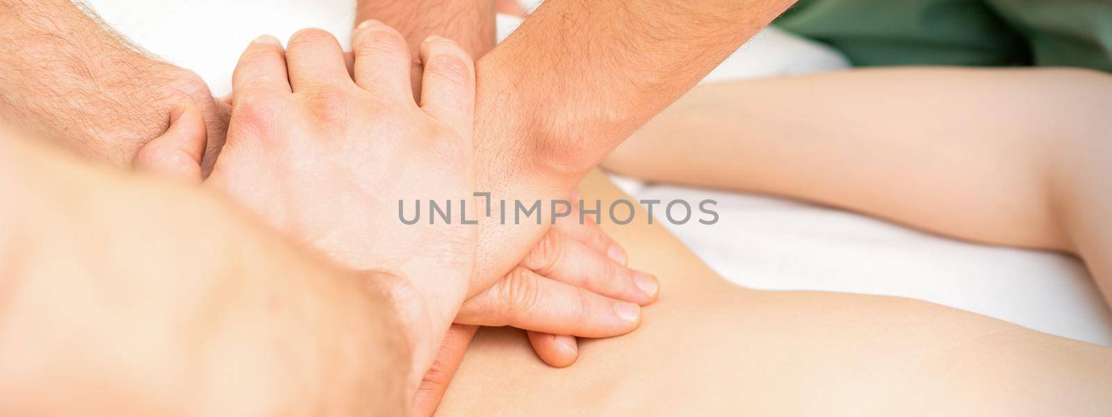 Young woman receiving a back massage in four hands by two masseurs at a spa salon