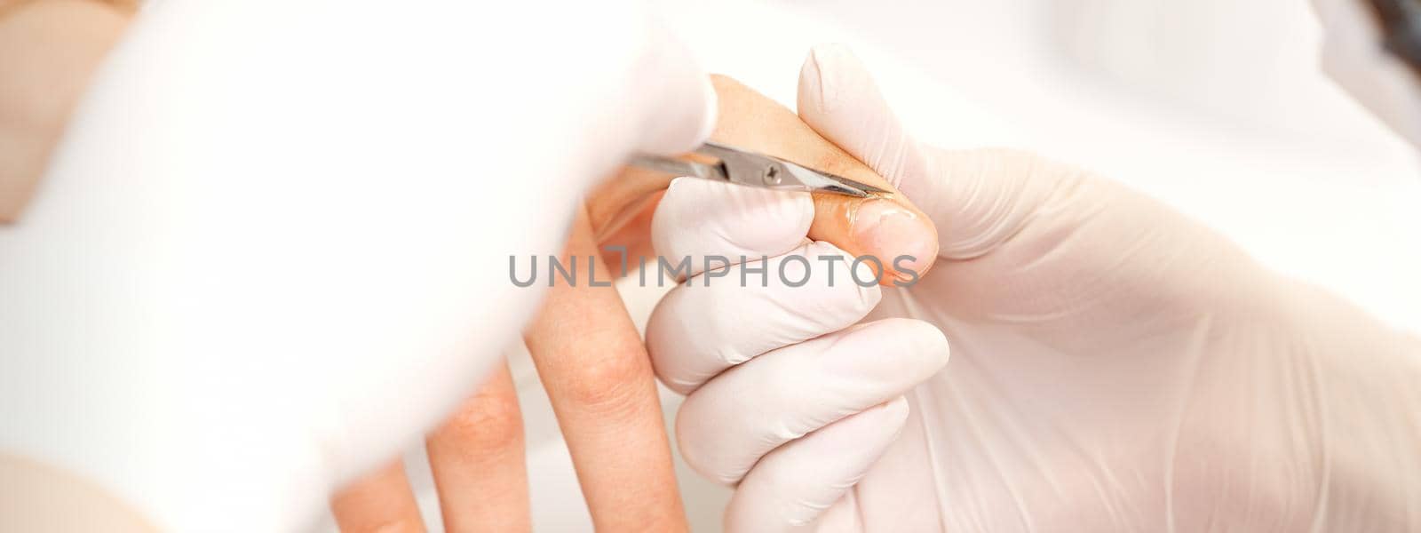 Close up of manicure master with manicure scissors removes cuticles of female nails at beauty salon