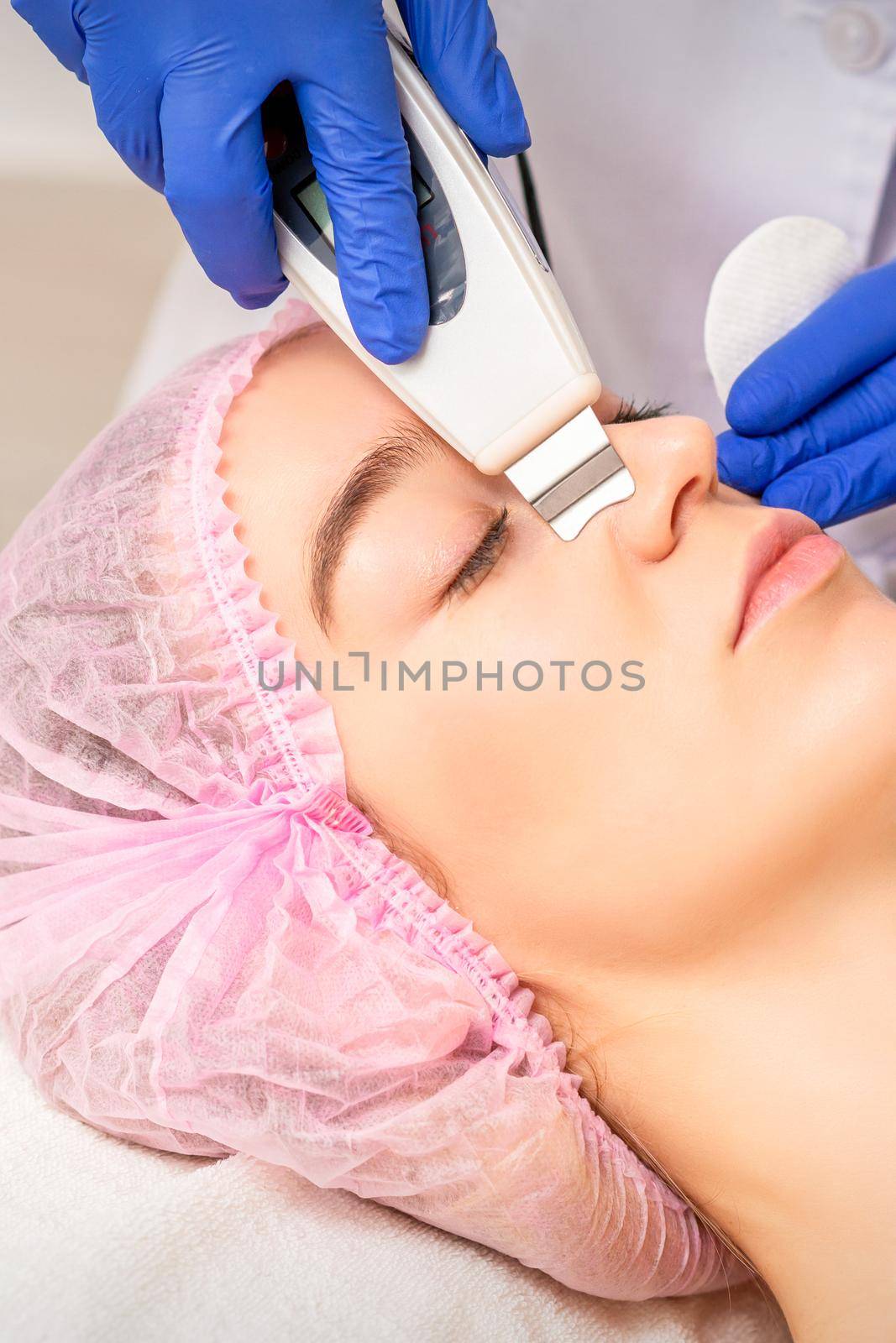 Closeup of beautiful young woman receiving ultrasound facial exfoliation and cavitation facial peeling with ultrasonic equipment in cosmetology office. by okskukuruza