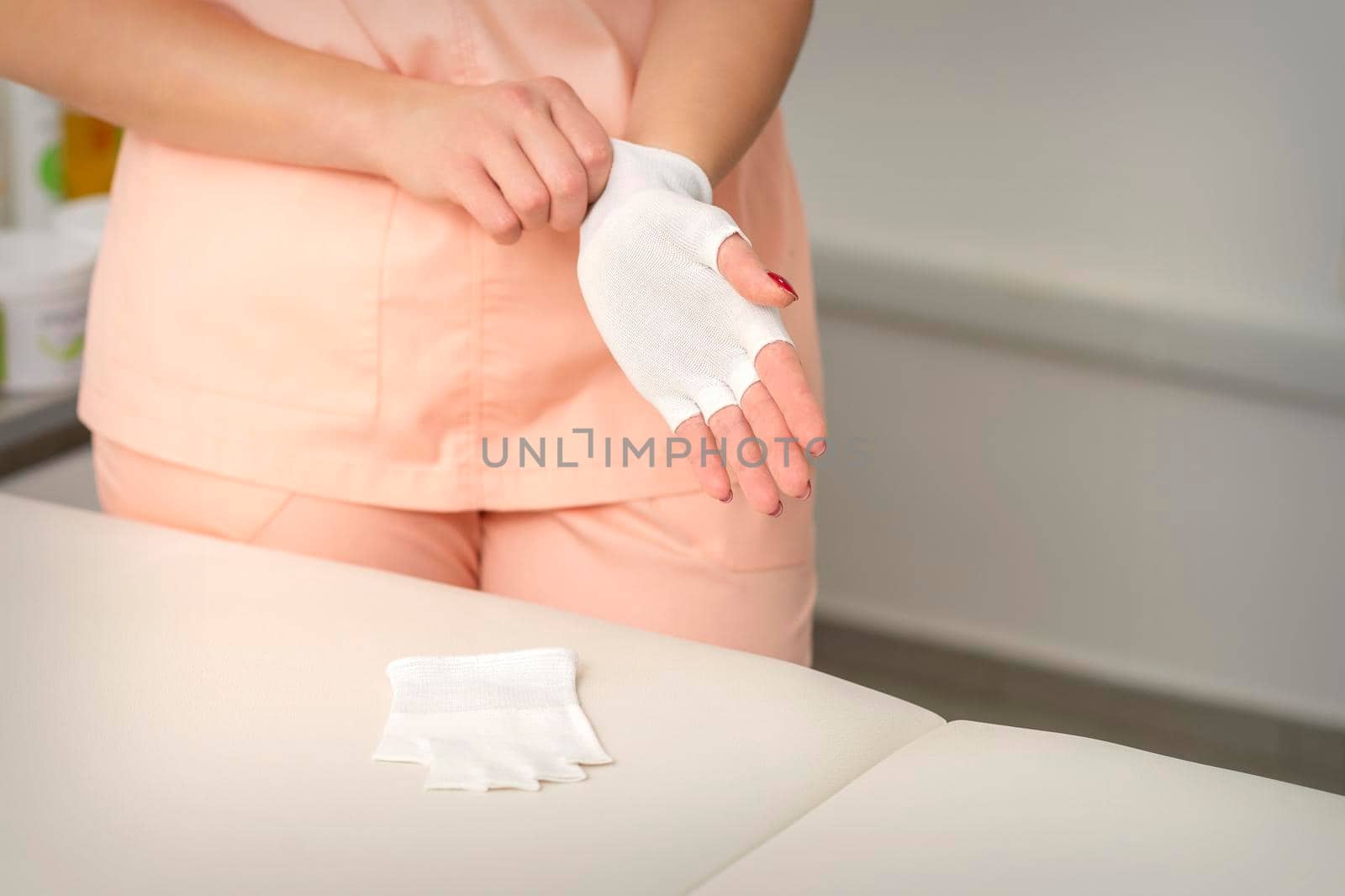 Cosmetologist in workwear wearing white bamboo fingerless gloves on her hands