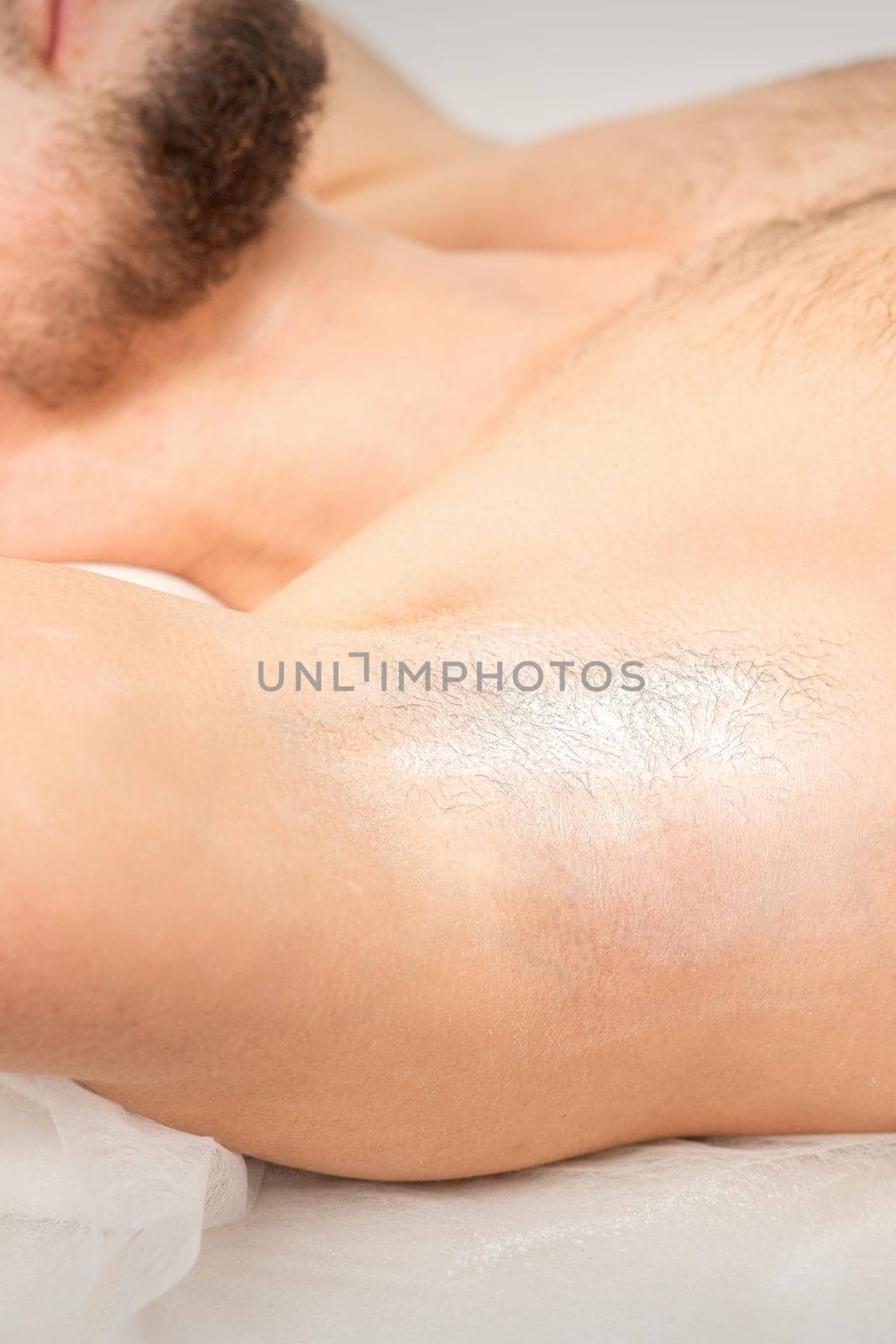 Young caucasian man receiving hair removal from his armpit in a beauty salon, depilation men's underarm